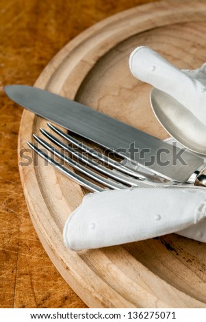 Silver knife fork and spoon with a white napkin and a rustic wooden plate
