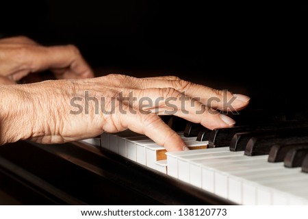 Old person\'s hands playing the piano. Close up view of skin texture and piano keys.