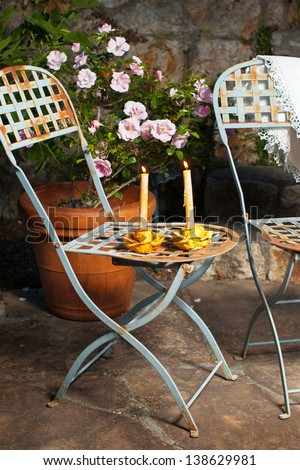 Romantic garden patio at night with lighted candles, pink roses and vintage blue French chairs
