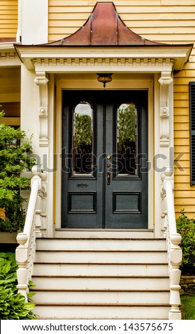 Front door of a vintage yellow house with white trim and a copper gable over the entry