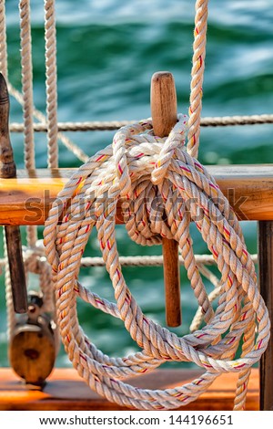 Sailboat close up of coiled rope secured to a wooden belaying pin on a schooner under sail with water in the background. Texture detail of rope and wooden fittings.