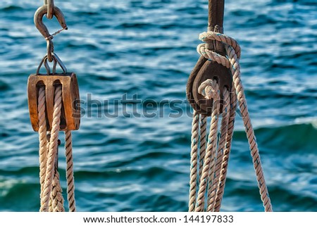 Detail shot of ropes and pulleys on a wooden schooner under sail, with blue water in the background