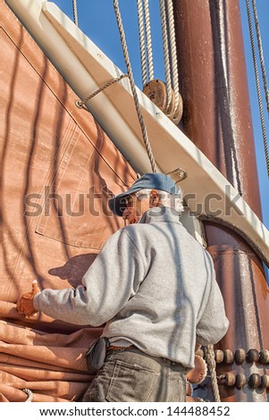 Active senior man on a sailing adventure trip, helps with the sail on a tall ship schooner. Concept for active retirement and maintaining good health.