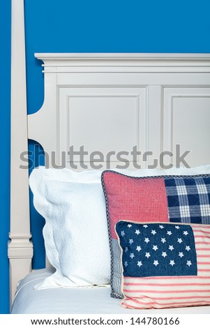 Wooden bed painted white against a blue wall. Pillows in a red, white and blue color theme.