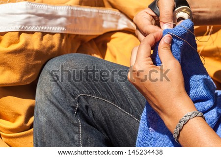 Deckhand on a big sailboat sews by hand to make repairs. Canvas sail cloth in the background.