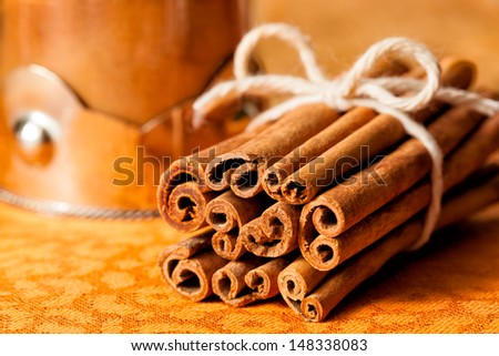 Cinnamon sticks tied in a bundle next to a decorative glass jar of the ground spice. Close up view with selective focus on the rolled ends.