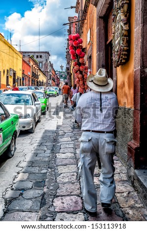 Cobblestone street in the picturesque town of San Miguel de Allende, Mexico. Street vendor carrying pole of candy apples for sale.