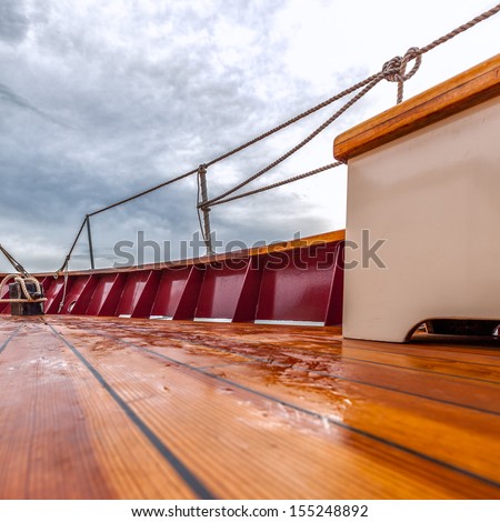 Wet wooden deck of a sailboat at sea under stormy skies. Square format with copy space. Shot from low vantage point.