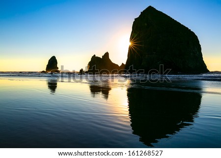 Silhouette of majestic sea stack rock formations at sunset with natural sun flare and reflections. Location: Haystack Rock, Cannon Beach, Oregon, USA