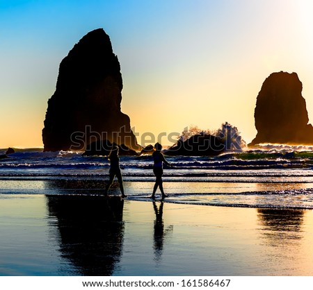 People walk at sunset on the beach in the wild Pacific Northwest with sea stacks dramatically backlit by the setting sun. Location: Stacks called 
