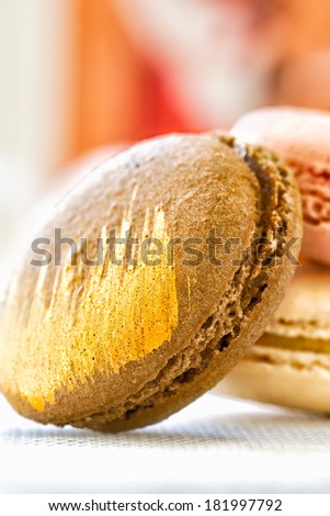 Macaroon decorated with edible gold icing. Close up with selective focus and background blur. Special occasion cookie with caramel filling.