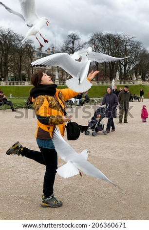 PARIS-JAN 4, 2014:An unidentified woman tosses food up in the air for birds to catch at the Luxembourg Gardens, a popular activity for visitors at the park, which is the 2nd largest in Paris.