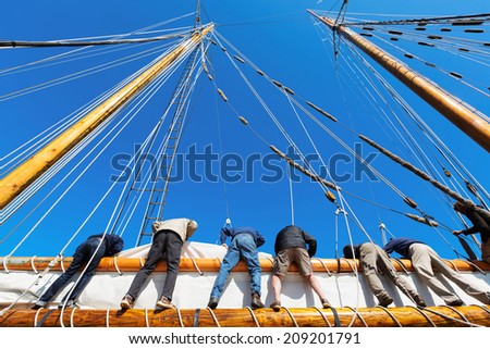 People working together to raise a big heavy sail on a tall ship at sea. Concepts: teamwork, cooperation, working toward a common goal, depending on each other