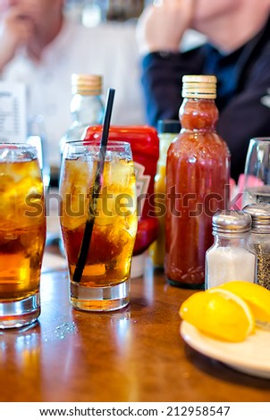 Restaurant table close up with selective focus on drinks and condiments. People in the background talking.