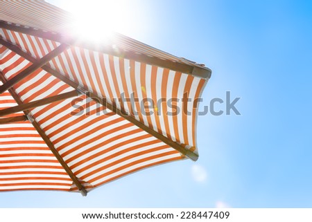 Orange and white striped beach umbrella with natural sun flare