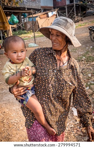 CAMBODIA-JAN 27, 2015: A smiling grandmother holds a small child on her hip and walks on a dirt road in a rural fishing village on the Mekong River. Unidentified people.