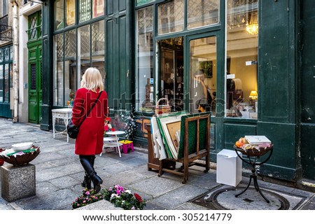 PARIS, FRANCE - JAN 3, 2014: Antique shop on a side street in the historic neighborhood of Le Marais. Items for sale on the sidewalk. An unidentified woman in a red coat walks by.