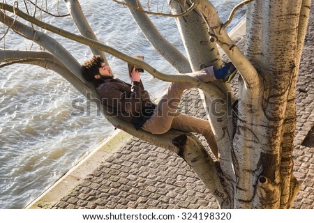 PARIS - Jan 2, 2014: A young man reading a book while reclining on a branch high up in a big tree on the bank of the Seine River, which is seen below.