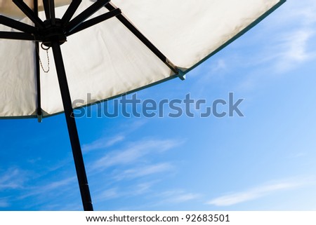 Looking up under big white beach umbrella against blue sky on a sunny day. White canvas with dark or black wood frame.  Room for text