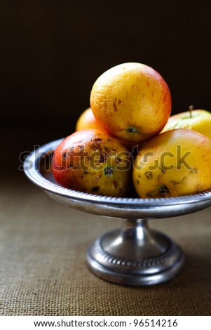 Bad rotten apples on a silver pedestal dish against black