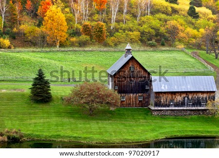 Beautiful old barn in a green meadow and trees with colorful fall leaves