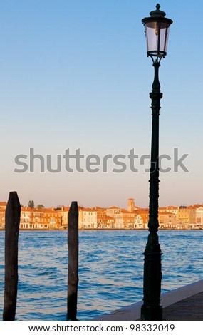 Venice, Italy at sunset, a lamppost silhouette at the water\'s edge.  Room for copy