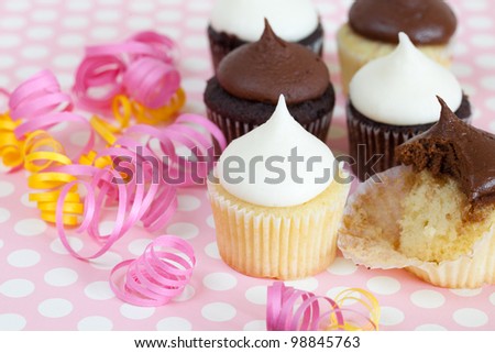 Chocolate and vanilla cupcakes with curled party ribbons on a polka dot background -- one cupcake is partly eaten