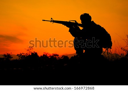 Silhouette shot of soldier holding gun with colorful sky and  mountain in background