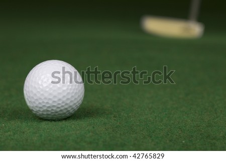 a golf ball and a golf putter are put on a indoor golf putting green