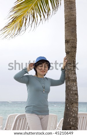 Pretty young Asian woman standing under a palm tree near sea