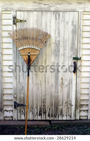 An old wooden rake leans against a dirty work shed.