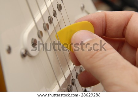 A hand holds a guitar pick and strums an electric guitar.