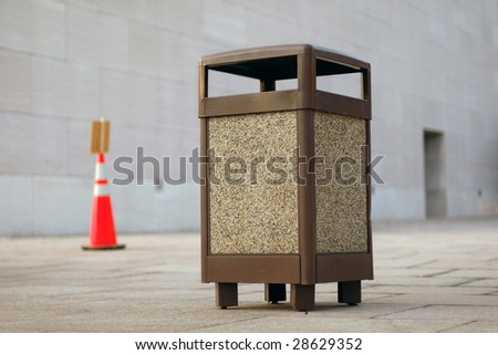 An open public space with brown garbage can in focus.