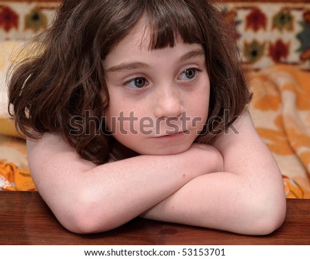 Serious cute little girl rests her head on crossed arms close-up