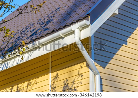 Tiles on the roof and rain gutter  on the house upholstered with siding.