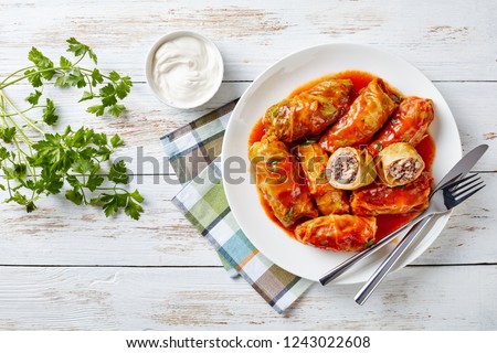 cabbage rolls stuffed with ground beef and rice served on a white plate on an old rustic table with sour cream in a bowl, view from above, close-up, flatlay