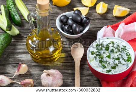 Tzatziki, cucumber, bottle of olive oil on old wooden table against the background of a cutting board