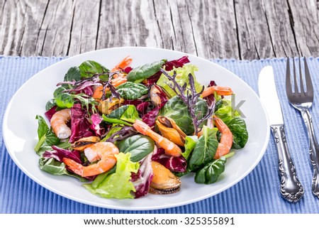 the best fresh salad of prawns, mussels and mixed lettuce leaves in the white dish on the old wooden table, rustic style, selective focus, macro, close-up