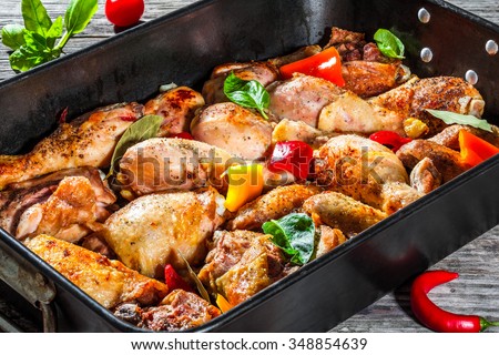 semi-fried chicken meat with colorful pieces of peppers, basil leaves and spices in the baking dish, preparing for baking in the oven for the festive dinner, view from above