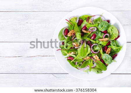 Mediterranean red beans salad with mix of lettuce leaves and walnuts on a white dish on a wood table with blank space left, italian style, close-up