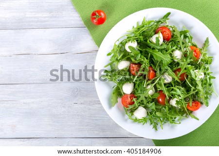 Dietary low calorie delicious salad with tomatoes, mini mozzarella, arugula on a white dish on a green table napkin,  studio light, overhead view
