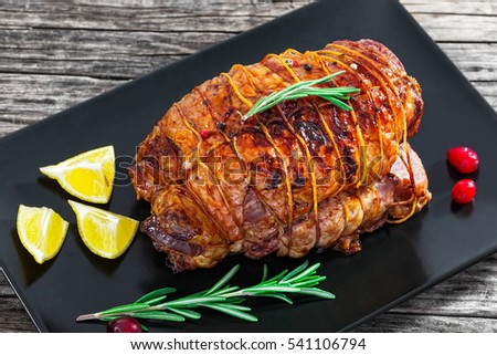 homemade turkey meat roulade roasted in oven on black rectangular dish with lemon wedges, rosemary and cranberry on dark old wooden table with kitchen towel, view from above, close-up