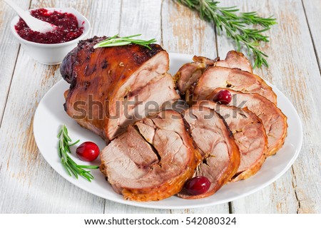 slices of delicious grilled turkey meat with cranberry and rosemary on white dish on old wooden table with berry sauce, view from above, close-up