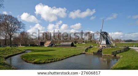 dutch panorama: windmill on a dike pumps water from low to high level out of the polder into the lake
