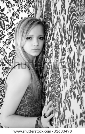 young female fashion model leaning against a white and black wall papered scene. image altered to black and white for a greater effect