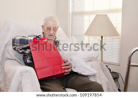A 94 year old elderly man, sitting alone in his apartment, opening a gift