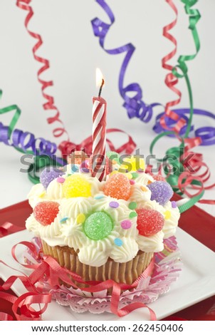 A delicious party cupcake with frosting and candies, with one lit candle, low light and selective focus on cupcake