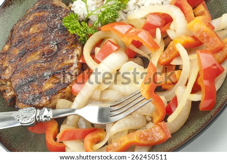 A plate of teriyaki grilled chicken with red peppers and cooked onions with white rice, closeup with full frame