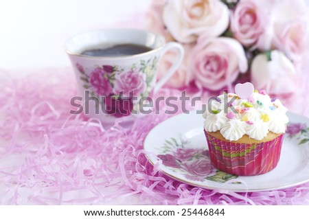 A pretty decorated cupcake with sprinkles and pink candy heart, with cup of coffee