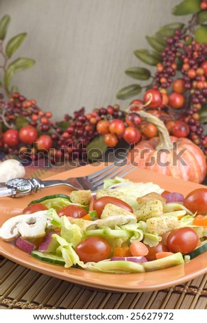 A fresh garden salad in an orange bowl with tiny pumpkins and fall colors in background  vertical with copy space